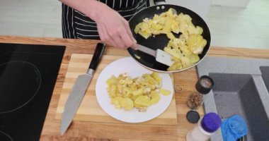 Dişi tavayı spatula kullanarak tavaya kızarmış patates döküyor. Önlüklü kadın akşam yemeğinde ağır çekimde yemek servisi yapıyor.