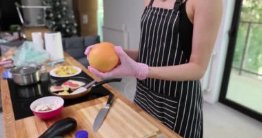 Önlüklü kadın mutfaktaki tezgahın üstünde olgun greyfurt tutuyor. Ev hanımı sağlıklı atıştırmalıklar için sulu meyve kesmeye hazırlanıyor.