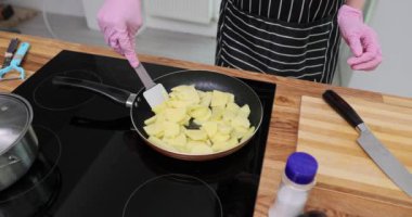 Kadın eli patatesleri elektrikli ocakta spatulayla karıştırır. Önlüklü ve eldivenli kadın akşam yemeği için lezzetli yemekler pişirir.