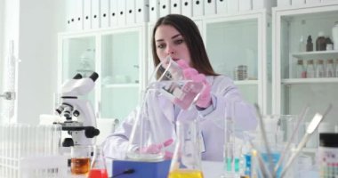 Kadın bilim adamı dikkatlice beher kabından temiz sıvı döküyor. Araştırmacı uygun teknik ve ölçümleri sürdürmek için her adımı izler