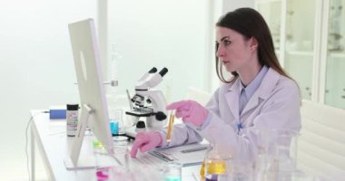 Kadın araştırmacı gözlemleri ve verileri bilgisayarda kaydeder. Bilimadamı deney tüpündeki sıvı reaksiyonunu önemli değişiklikler için inceliyor.