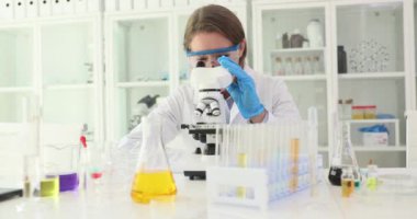 Kadın bilim adamı çağdaş mikroskobu yavaş çekimde inceliyor. Kadın araştırmacı ince özellikleri ve verileri ortaya çıkarmak için titizlikle örnekleri analiz eder.