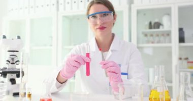 Kadın bilim adamı üzerinde çalışılan pembe sıvı ve reaktif örneklerle tüp sunar. Kadın araştırmacı modern laboratuardaki araştırmaların önemini gösteriyor.