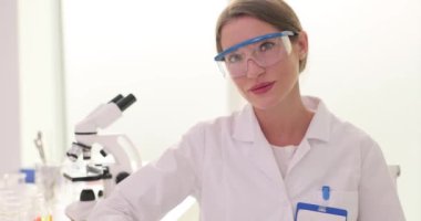 Kadın bir laboratuvar çalışanı detaylara dikkat eden kağıtlarla oturuyor. Koruyucu gözlüklü kadın bilim adamı doğru bilgiyi elde etmek için belgeleri kullanıyor.