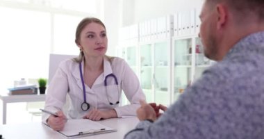 Kadın doktor, hastanın semptomları anlattığı gibi dikkatlice dinler. Erkek hasta muayene sırasında semptomların yoğunluğunu ve süresini tanımlar.