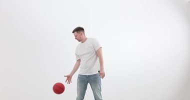 Adam ışık odasında top sürüp, egzersiz yapıyor. Kot pantolonlu sakallı bir sporcu spor salonundaki becerilerini yavaş çekimde eğitir. Etkin yaşam biçimi