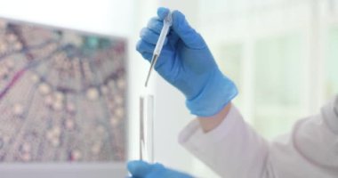 Kadın işçi laboratuardaki tüpte sıvı transferi için pipet kullanıyor. Bilim adamları deneysel ölçümlerin doğruluğunu korumak için ellerinin titrememesi gerekir.