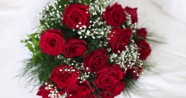 Kırmızı güllerden yapılmış albenili düğün buketi yatakta yatıyor. Aşk ve tutkunun canlı kırmızı gülleri. Çiçeklerin tatlı kokusu odayı dolduruyor.