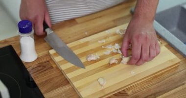 Erkek eller, karanfil parçalamak için bıçağı kullanarak sarımsağı kesme tahtasına bastırıyor. Adam tezgahta yemek pişirmek için aromatik malzeme hazırlar.