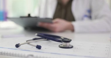 Doktor, iş yerinde steteskop ve takvimle duran, elinde not panosu olan kağıtları inceliyor. Üniformalı doktor hastanın tıbbi geçmişini kontrol ediyor.