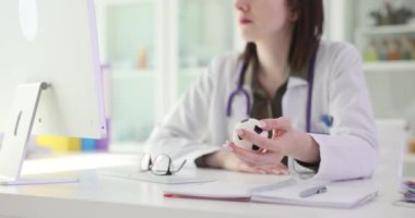 Steteskoplu kadın doktor hastanedeki iş yerinde elinde stres önleyici topla oturuyor. Odaklanmış kadın bilgisayarda tıbbi geçmişi okuyor.