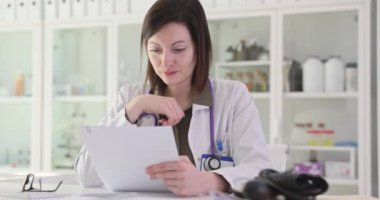 Endişeli kadın doktor test sonuçlarını dikkatle okur. Tıp çalışanı, hastalarla bulguları ve sonuçları tartışmaya hazırlanan verileri yorumluyor