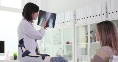 Doktor hastanın ayaklarının röntgenini ve eklem ağrısının yavaş çekimini sunar. Tıp çalışanı ilgili ayrıntılara dikkat çekiyor ve tedavinin uygulanmasını netleştiriyor