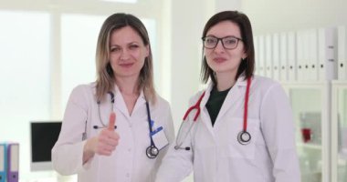 Kadın doktorlar onaylama jestinde başparmak göstererek gülümserler. Kadınlar çalışmanın sonucu veya kararın paylaşımı ile güven ve memnuniyeti yansıtır