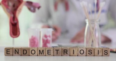 Jinekoloğa karşı tahta küplerden yapılan kelime endometriyozisi. Doktor iş yerinde ilaç ve rahim modeliyle evrak işleriyle uğraşıyor.