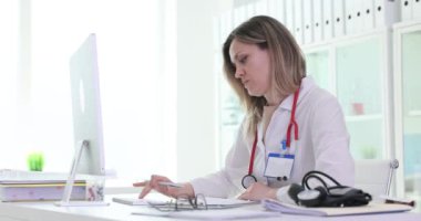Kadın doktor, hastanedeki iş yerindeki monitöre bakarak evrak işleriyle uğraşıyor. Kadın doktor bilgisayar hazırlama raporundan veri yazar