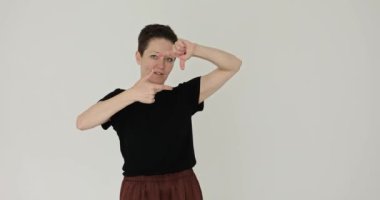 Esmer kadın kamera görüntüsünü gri arka planda parmaklarıyla çekiyor. Kadın, doğru perspektifi yavaş çekimde yakalama maksadıyla mükemmel açıyı görselleştirir.
