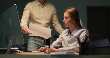 Bayan patron raporlarda yanlış verilere öfkeyle tepki verir. Saçları dökülmüş bir kadın yönetici, hayal kırıklığı yüzünden meslektaşına buruşmuş kağıt atıyor.