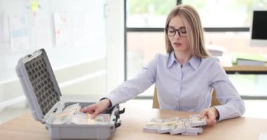 İş kadını şirket ofisindeki iş yerinde otururken bavula banknotlar koyar. Genç bayan güvenli bankada depolama için para hazırlıyor.