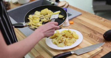 Mutfak spatulasıyla tabakta servis edilen sebzeli kızartma tavasını elinde tutan kişi. Önlüklü aşçı akşam yemeği için lezzetli yemekler hazırlar.