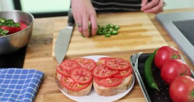 Kadın eli domatesli sandviçlerin üzerine doğranmış yeşil biber koyar. Kadın mutfaktaki sağlıklı malzemelerden lezzetli atıştırmalıklar hazırlıyor.