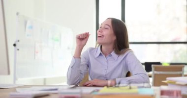 Bayan ofis müdürü hayali mikrofonda şakalaşıyormuş gibi yapıyor. Oyuncu hareket, işi eğlence ve yoldaşlık anlarıyla dengeleme becerisini vurguluyor