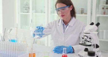 Laboratuvardaki kadın suyu şişeden ölçü kabına aktarıyor. İşçi dikkatli yaklaşımı araştırma faaliyetlerinde hassasiyetin önemini vurgular