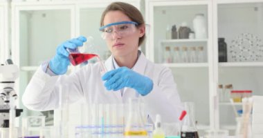 Kadın bilim adamı ölçülü miktarda sıvıyı test tüpüne boşaltıyor. Nitelikli bilim adamı kırmızı sıvıyı ağır çekimde analiz için hazırlıyor.