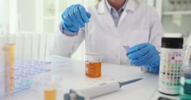 Araştırmacı laboratuvara mor reaktör ekleyerek turuncu sıvıyı karıştırıyor. Kimyager, iş yerinde karışımı kontrol eden sıvıları birleştirir