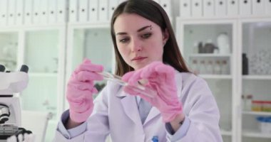 Yoğunlaşmış kadın bilim adamı laboratuardaki cam tüpten alınan numunelerle madde örneği alıyor. Tıp bilimadamı biyolojik materyalleri araştırıyor