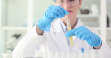 Bilim kadını laboratuarda PH bandı olan test tüpünün içeriğini inceliyor. Kimyager laboratuvarda reaksiyonlarla sıvı madde incelemesi yapar.