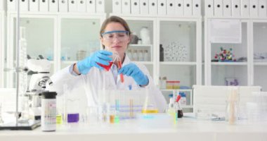 Kadın araştırmacı, iş yerindeki deney tüpünden kırmızı sıvıyı test tüpüne döküyor. Kadın kimyager laboratuarda deneyler için malzeme hazırlıyor.