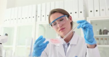 Kadın asistan, laboratuardaki pipetle çok iyi numune tepsisine sıvı damlatıyor. Kimyager laboratuvarda sıvı numuneleriyle testler yapar.