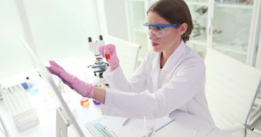 Kadın teknisyen tıp laboratuarında bilgisayar ekranına dokunan verileri analiz ediyor. Masa başındaki bilgisayar üzerinde sıvı şişesi deneyinde asistanım.