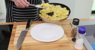 Deneyimli aşçı elinde kızartma tavası ve yanında beyaz tabakta spatulayla kızarmış patates dilimleri tutuyor. Taze kızarmış patateslerin hoş kokusu havayı ağır çekimde doldurur.