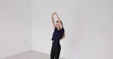 Genç bir kadın stüdyoda paspasın üzerinde ısınma egzersizi yapıyor. Kadın sporcu vücut şeklini yavaş çekimde iyileştirmek için spor yapıyor.