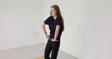 Saçları dökülmüş genç bir kadın atölyede dans figürleri yapıyor. Sportif dişi, vücudun esnekliğini, zarif hareketleriyle yavaş çekimde gösterir.