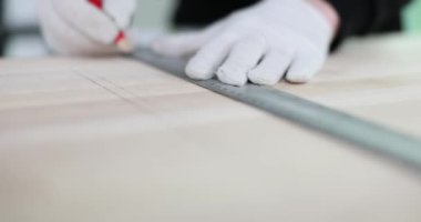 İşçi elleri metal cetvel tutuyor. Tahtaya kurşun kalemle tabela yapıyorlar. Eldivenli çalışan, odun kesmek için doğru ölçümler yapar.