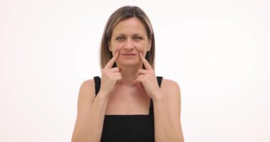 Üzgün kadın, stüdyoda parmakları beyaz arkaplanda gülümseme yaratıyor. Üzgün kadın, mutluluğu yavaş çekimde taklit eden negatif duygularla başa çıkmaya çalışır.