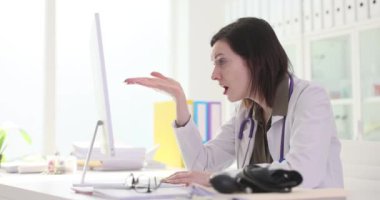 Kadın doktor, ofis mobilyalarına karşı yorgunluk gösteren bilgisayar ekranına bakıyor. Üniformalı kadın doktor hastanede çalışmaktan yoruldu.