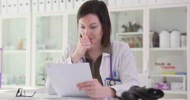 Odaklanmış kadın doktor, iş yerinde oturan sağlık raporunu inceliyor. Üniformalı kadın, randevudan sonra hasta için etkili tedavi planı arıyor