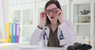 Yorgun kadın doktor hastanedeki iş yerinde gözlük çıkartıyor. Üniformalı kadın doktor, uzun süreli ağır çekimin ardından yorgunluğunu dile getiriyor.