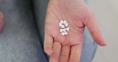 Kadın, koltukta oturan avuç içinde kalp şeklinde haplar gösteriyor. Kadının evinde kardiyovasküler sistem için vitamin var. Sağlık için tıbbi takviyeler