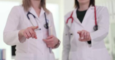 Kadın doktorlar kameraya işaret ederek hastanede güven ve profesyonellik gösteriyorlar. Sağlık hizmetlerinde takım çalışması ve destek