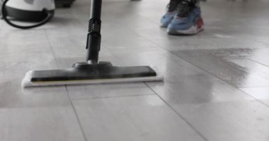 Temizlikçi ev ortamında zemini dezenfekte etmek için buhar paspası kullanıyor. Profesyonel olarak oturma odasının temizliğini sağlamaya odaklanmış.