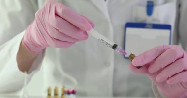 Pembe eldivenli hemşire klinikteki tehlikeli bir hastalığın aşısını şırıngayla dolduruyor. Sağlık çalışanı hastane ofisinde enjeksiyona hazırlanıyor.