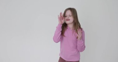 İyimser kız beyaz arka planda el hareketlerini taklit etmeye çalışıyor. Pembe kazak giymiş gevşek saçlı çocuk müzik eşliğinde el kaldırır.