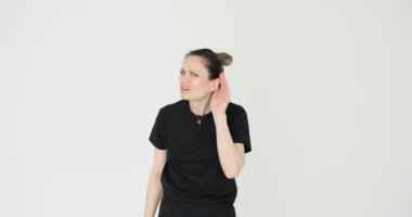 Kadın el ele tutuşup beyaz arka plandaki dedikoduların zayıf seslerini yükseltmeye çalışıyor. Meraklı kadın konuşmanın kilit noktalarını duymaya çalışır.