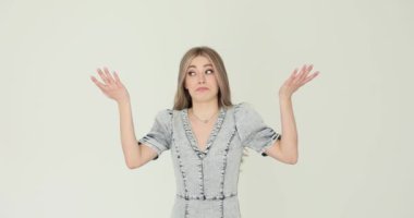 Sıradan kot elbiseli, şaşırmış genç bir kadın beyaza şaşkınlığını ifade etmek için elini kaldırıyor. Bayan duygularını anlamlı jestlerle gösterir.