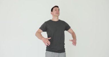 Spor giyim bölümündeki genç adam ziyaretçileri beyaz arka planda hoş geldin jestleriyle selamlıyor. Dost canlısı erkek sporcu spor salonundaki yeni müşterileri duygusal olarak karşılıyor.